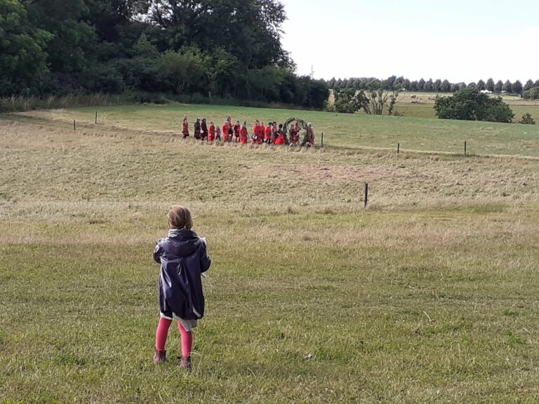 Kind auf weiter Wiese schaut der Prozession aus der Ferne zu.